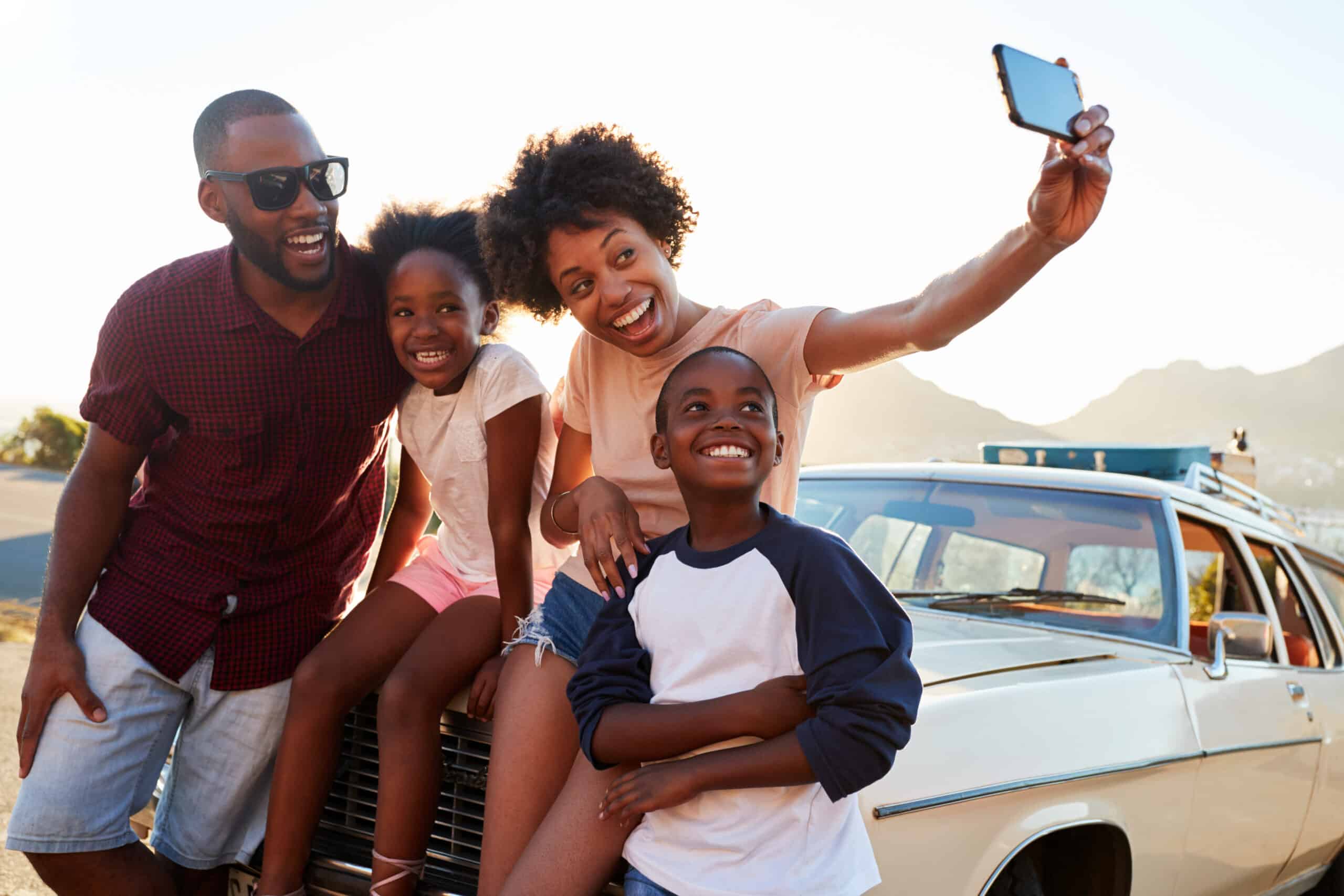 Family posing for a selfie next to a car packed for a road trip