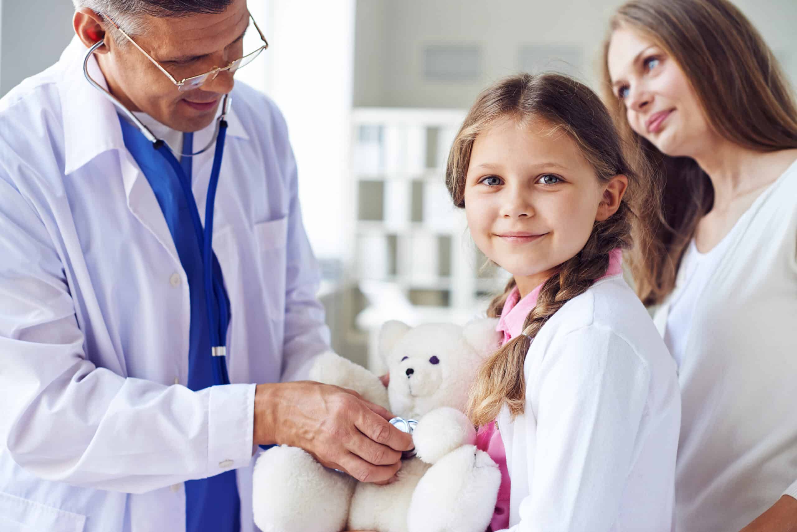 Little girl with teddy bear visiting doctor