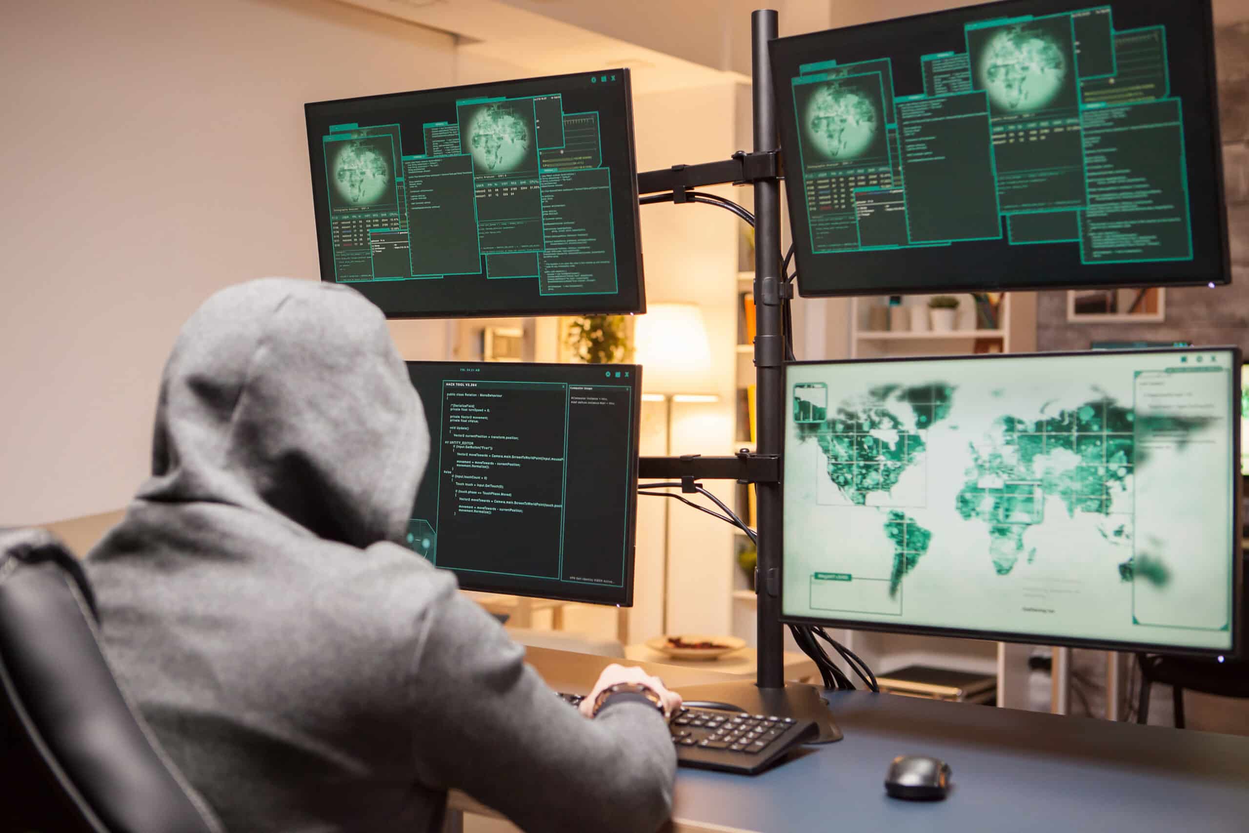 Dangerous hacker wearing a hoodie while planting a malware from computer with multiple screens.